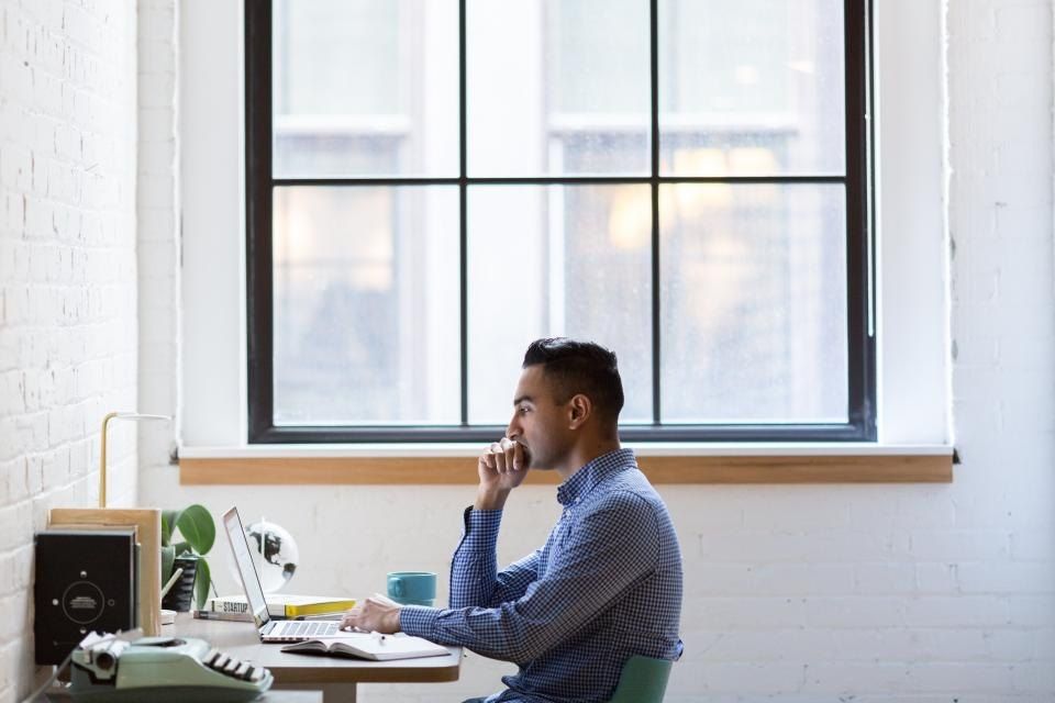 A student thinking at a desk by a large window